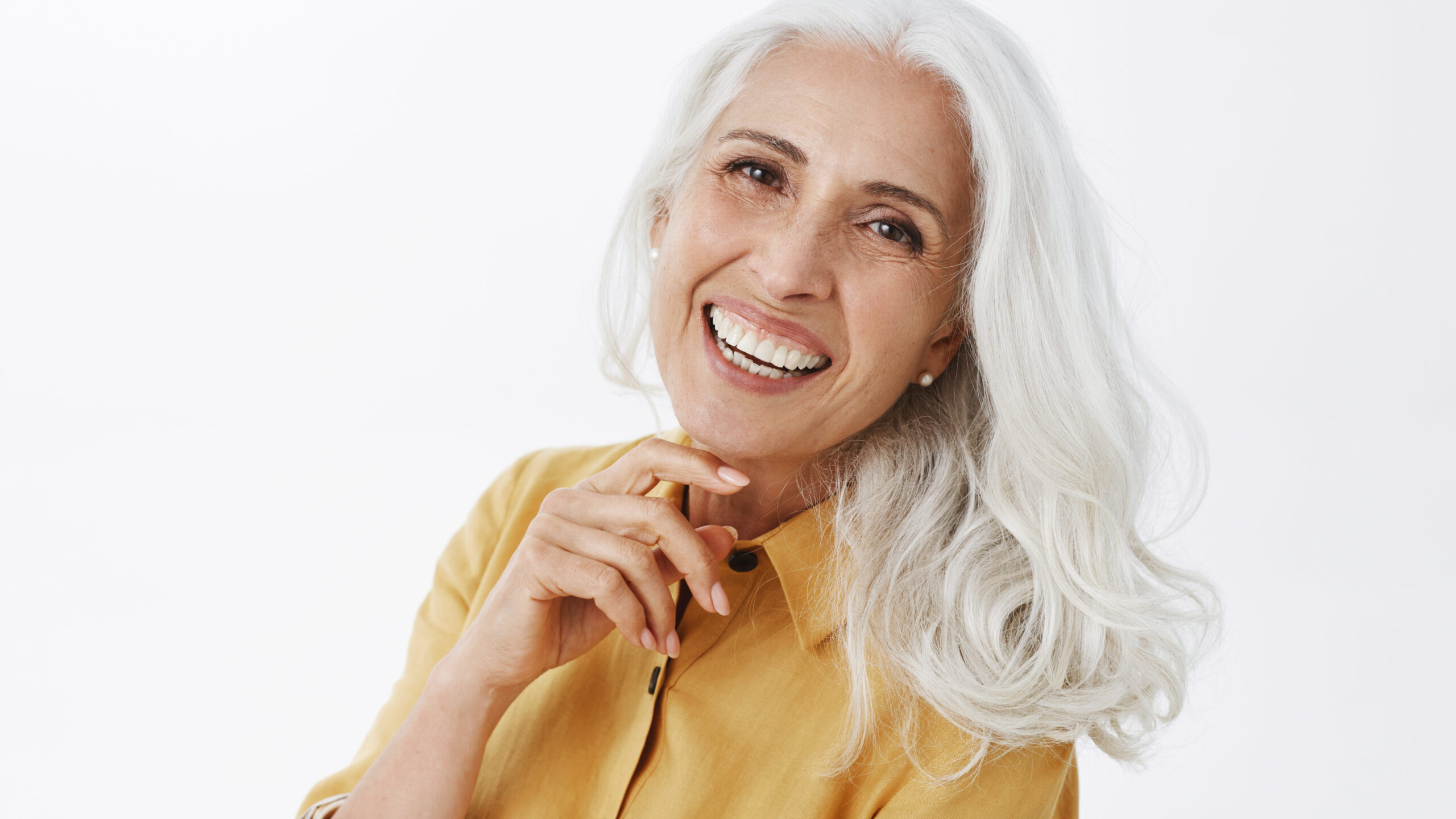 Close-up shot of happy delighted and accomplished charming european elderly female with white hair in yellow trench coat touching face gently laughing from joy feeling pretty and energized
